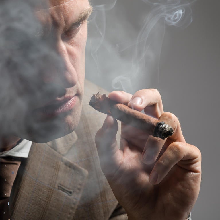 A well-dressed man smokes a cigar